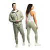 A man and woman standing side by side in matching heather sage green Bickford USA athletic wear — the man wears the Athletic Hooded Quarter Zip with joggers and white sneakers, and the woman is shown from the back in high-waisted leggings paired with a white racerback tank top and white sneakers, against a white background.
