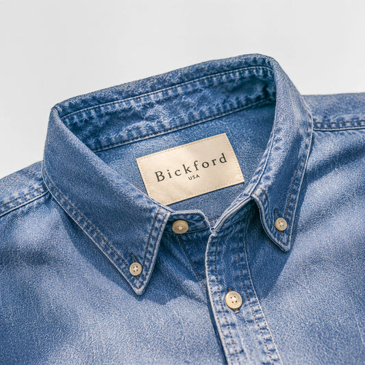Close-up detail of the Bickford USA Denim Field Shirt collar, showing the button-down collar points with cream buttons, contrast stitching, and a cream Bickford USA woven label at the neck, against a light gray background.