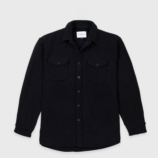Bickford USA button-down fleece overshirt in black, flat lay front view, featuring a spread collar, dual chest pockets with button flaps, a full front button placket with matte black buttons, and a curved hem, against a light gray background.