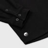 Close-up detail of the cuff and lower hem of the Bickford USA black button-down fleece overshirt, showing the two-button barrel cuff, matte black buttons, and a circular woven Bickford logo patch on the lower left hem.