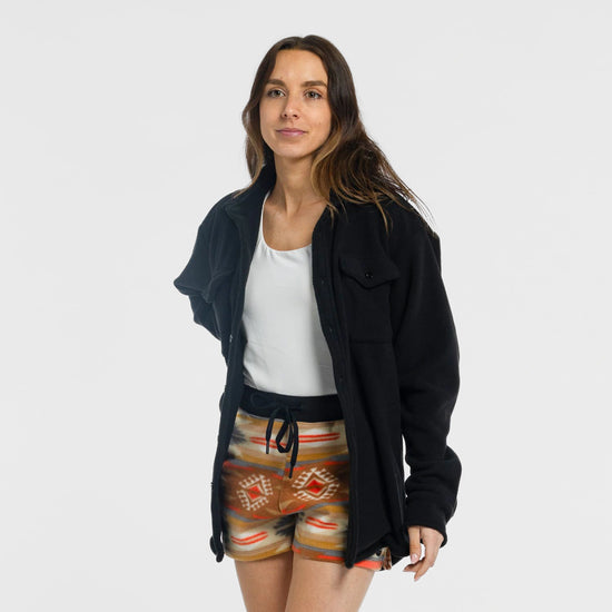 Woman wearing the Bickford USA black button-down fleece overshirt open over a white tank top and Heritage Trail colorway fleece shorts, facing forward and smiling, against a white background.