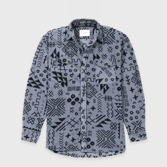 Bickford USA button-down fleece overshirt in the Boulder colorway — a gray base with an allover black geometric and tribal print — flat lay front view, featuring a spread collar, dual chest pockets with button flaps, a full button placket with dark buttons, and a curved hem, against a light gray background.