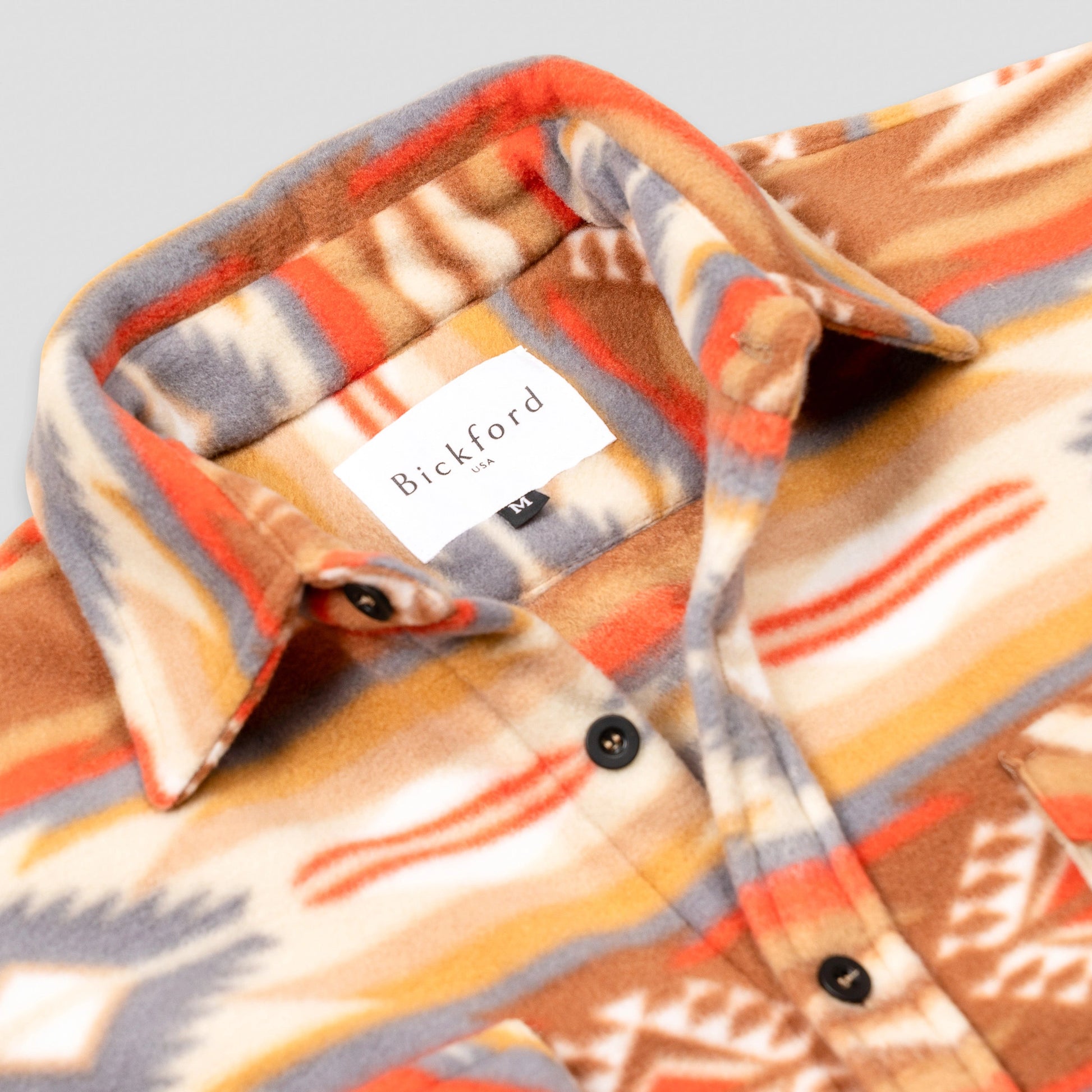 Close-up detail of the open collar and upper chest of the Bickford USA Heritage Trail colorway button-down fleece overshirt, showing the spread collar, Bickford USA size M label inside the neck, and dark button placket.