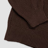 Close-up detail of the dark brown Fisherman sweater showing the folded hem and cuff, highlighting the contrast between the seed stitch body and the ribbed knit trim.