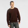 Man wearing the Bickford USA Fisherman sweater in dark brown, paired with medium-wash denim jeans, shown from the waist up against a light gray background.