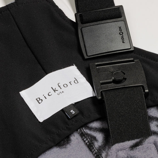 Close-up detail of a Bickford USA label with size S tag and Fidlock magnetic buckle hardware on the Boulder colorway overall bib, with the black interior lining visible.