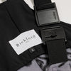 Close-up detail of a Bickford USA label with size S tag and Fidlock magnetic buckle hardware on the Boulder colorway overall bib, with the black interior lining visible.
