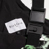 Close-up detail of a Bickford USA label with size S tag and Fidlock magnetic buckle hardware on the Eastern Pine colorway overall bib, with black interior lining and green-print fleece visible.
