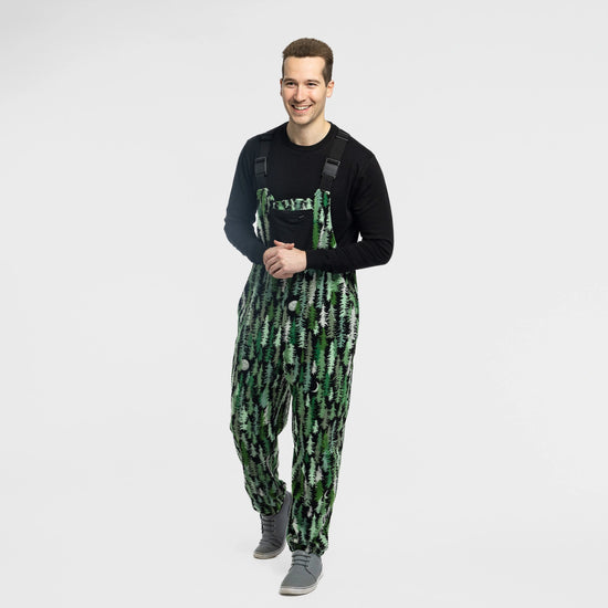 Man wearing the Bickford USA Eastern Pine colorway fleece overall bib over a black long-sleeve shirt, with gray sneakers, hands clasped and smiling, against a white background.