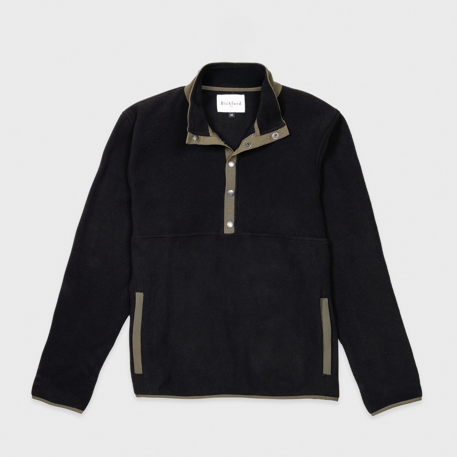 Bickford USA quarter-snap fleece pullover in black, flat lay front view, featuring an olive green grosgrain placket with silver snap buttons, matching collar trim and side pocket trim, against a light gray background.