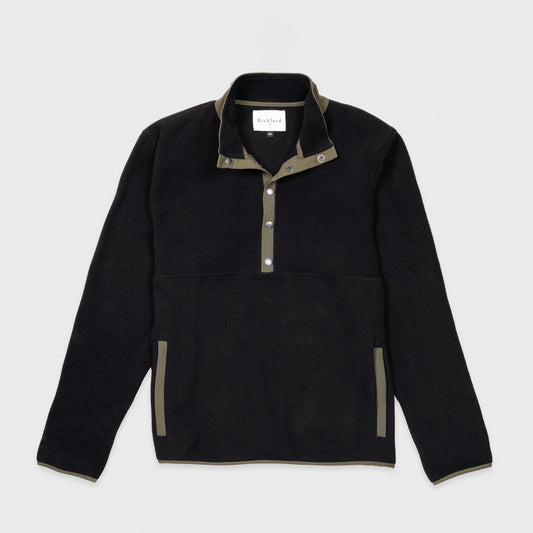Bickford USA quarter-snap fleece pullover in black, flat lay front view, featuring an olive green grosgrain placket with silver snap buttons, matching collar trim and side pocket trim, against a light gray background.
