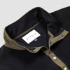 Close-up detail of the collar and snap placket on the Bickford USA black quarter-snap fleece pullover, showing the olive grosgrain trim, silver snap buttons, and Bickford USA size M label inside the collar.