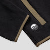 Close-up detail of the hem and side pocket of the Bickford USA black quarter-snap fleece pullover, showing the olive grosgrain pocket trim and a circular woven Bickford logo patch on the lower left hem.