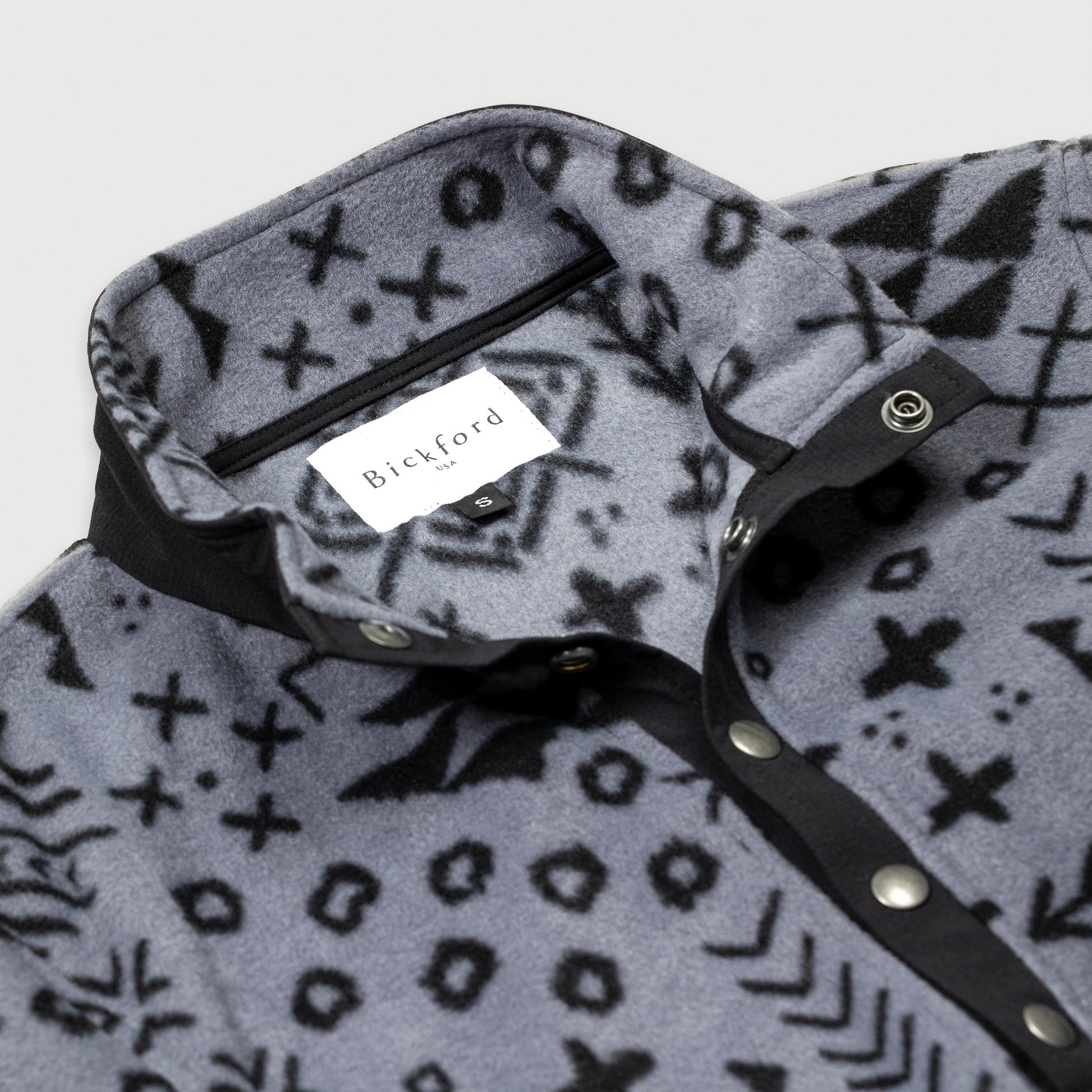 Close-up detail of the open collar and snap placket on the Bickford USA Boulder colorway quarter-snap pullover, showing the black grosgrain trim, silver snap buttons, and Bickford USA size S label inside the collar.
