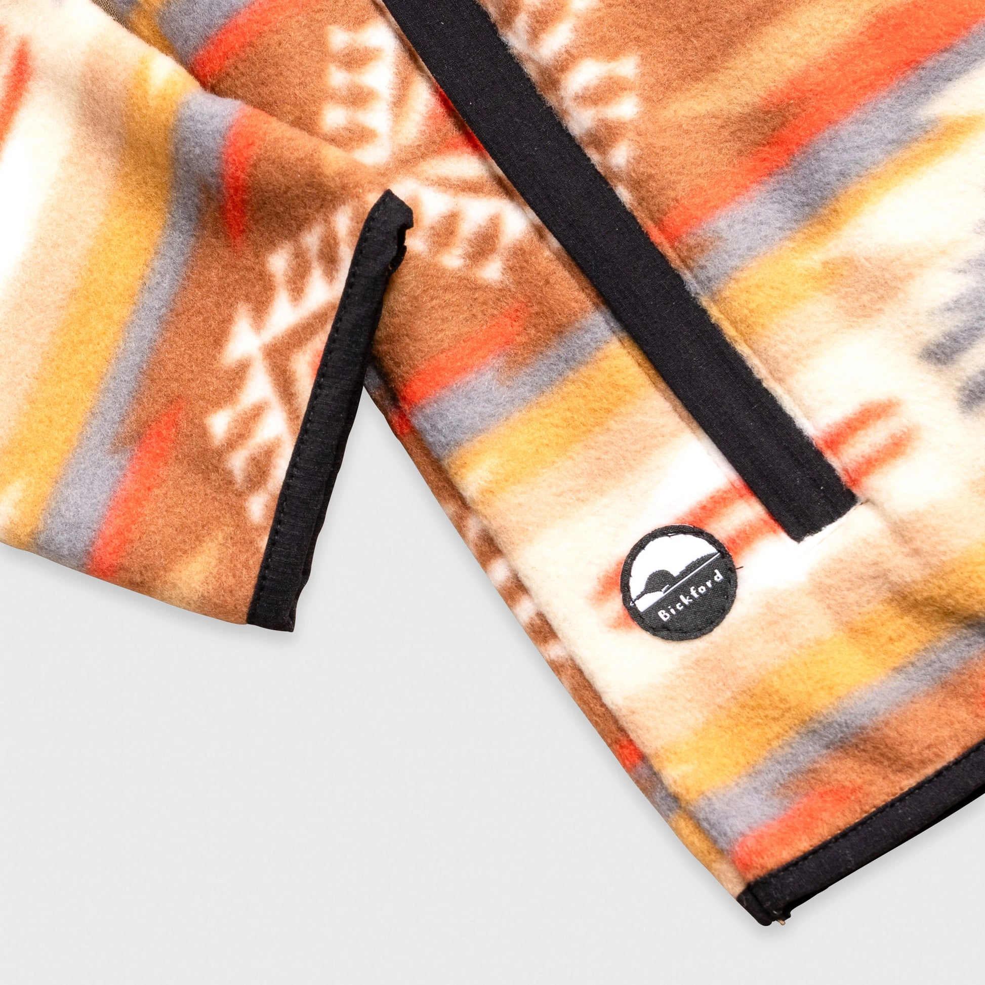 Close-up detail of the hem and side pocket area of the Bickford USA Heritage Trail colorway quarter-snap pullover, showing the black grosgrain trim and a circular woven Bickford logo patch on the lower left hem.