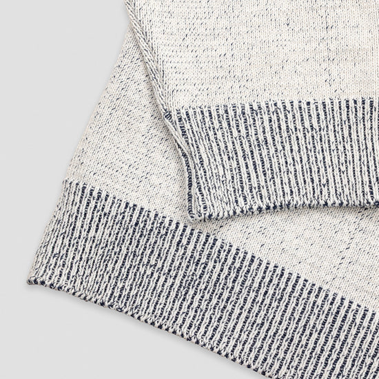 Close-up detail of The 1926 Sweater in natural and grey showing the folded hem and cuff, highlighting the contrast between the marled natural knit body and the grey and white striped ribbed trim.