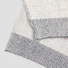 Close-up detail of The 1926 Sweater in natural and grey showing the folded hem and cuff, highlighting the contrast between the marled natural knit body and the grey and white striped ribbed trim.