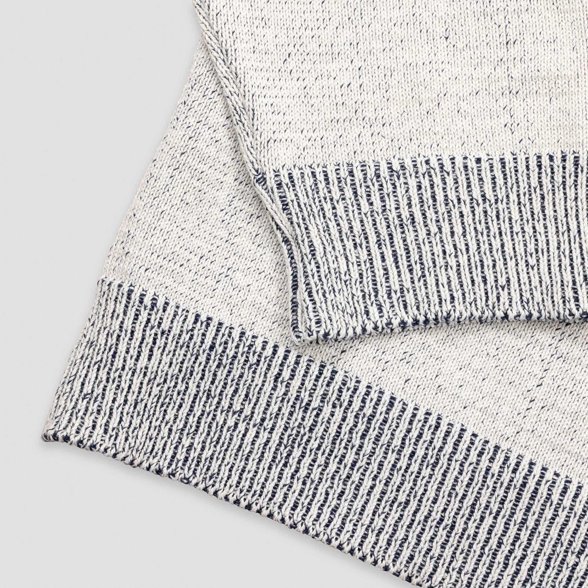 Close-up detail of The 1926 Sweater in natural and grey showing the folded hem and cuff, highlighting the contrast between the marled natural knit body and the grey and white striped ribbed trim.