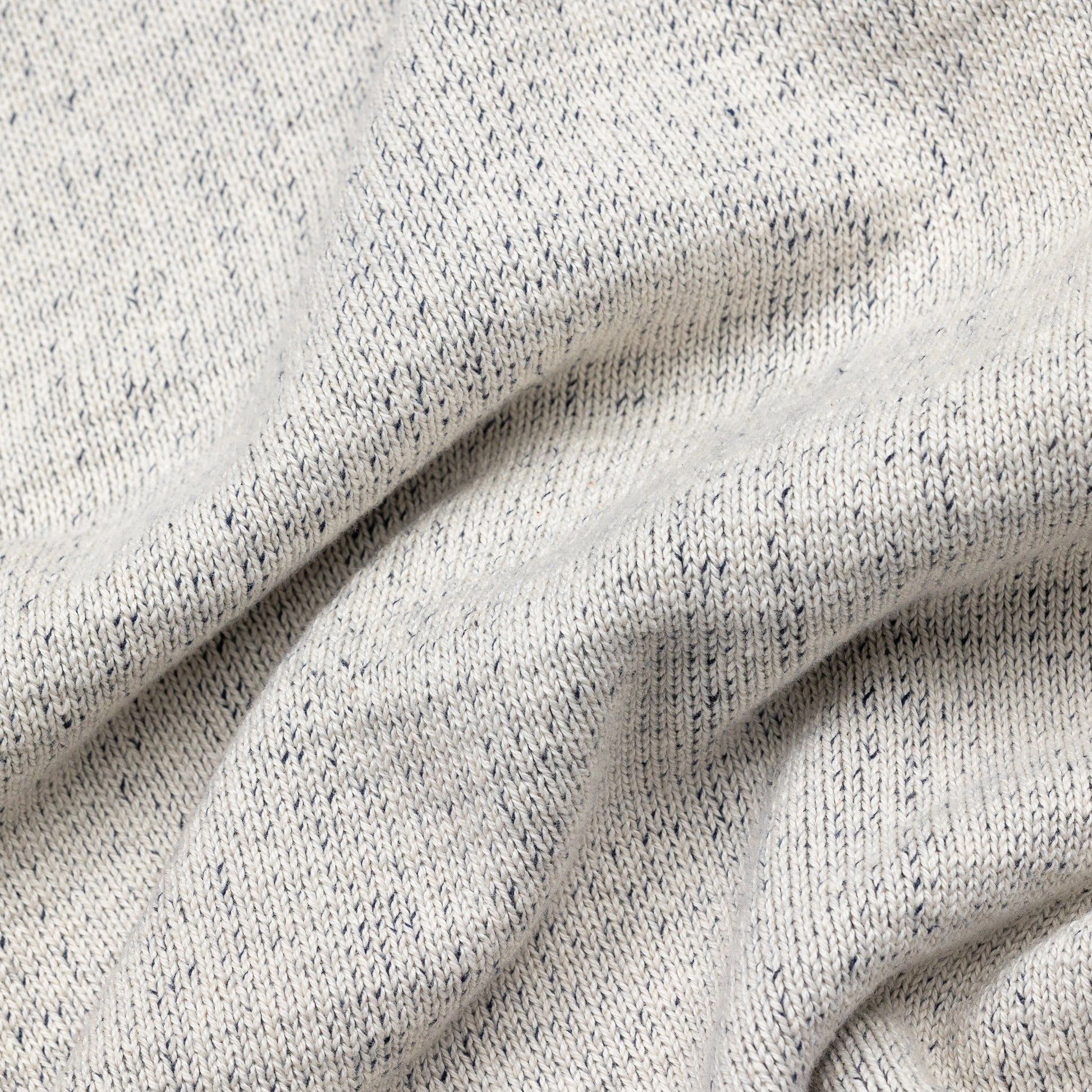 Extreme macro close-up of The 1926 Sweater fabric in natural and grey, showing the fine marled knit texture with natural cream yarn flecked throughout with dark grey.