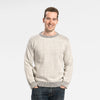 Man wearing Bickford USA The 1926 Sweater in natural and grey, paired with dark wash denim jeans, shown from the waist up against a light gray background with hands in pockets.