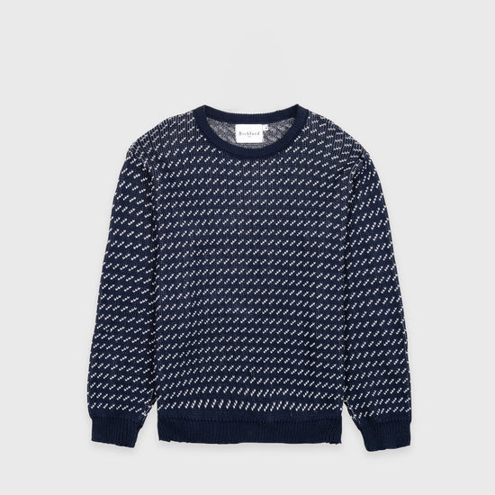 Bickford USA The 1926 Sweater in navy and natural, laid flat on a light gray background, showing the full front with an all-over diagonal birdseye knit pattern in navy and white and a solid navy ribbed crew neck, cuffs, and hem.