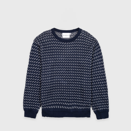 Bickford USA The 1926 Sweater in navy and natural, laid flat on a light gray background, showing the full front with an all-over diagonal birdseye knit pattern in navy and white and a solid navy ribbed crew neck, cuffs, and hem.