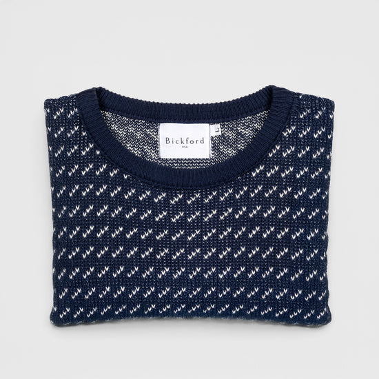 Bickford USA The 1926 Sweater in navy and natural, neatly folded and photographed from above, with the Bickford USA label visible at the center of the solid navy ribbed neckline and the birdseye pattern visible on the body.