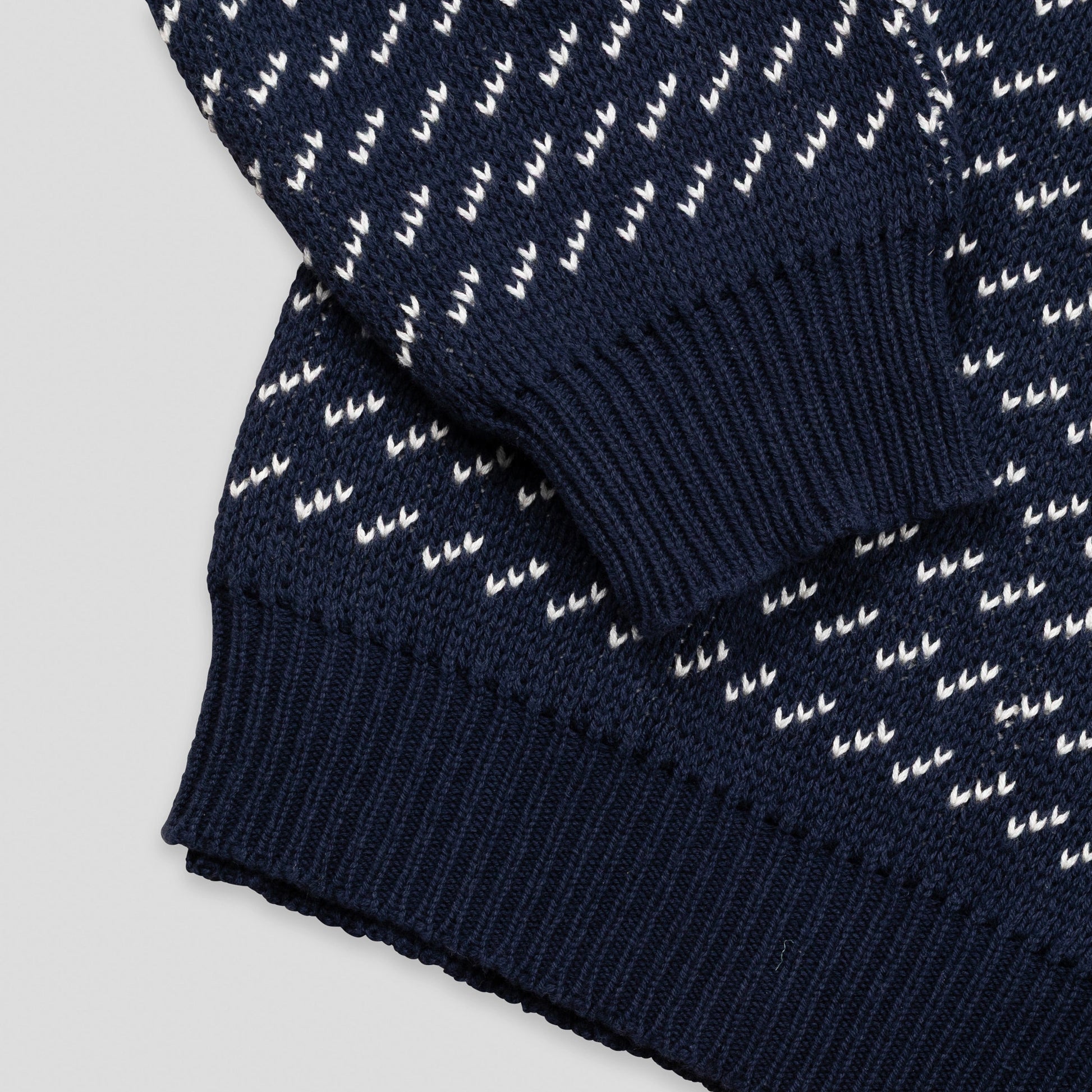 Close-up detail of The 1926 Sweater in navy and natural showing the folded hem and cuff area, highlighting the contrast between the diagonal birdseye patterned body and the solid navy ribbed trim.