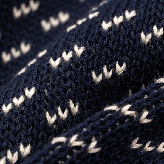 Extreme macro close-up of The 1926 Sweater fabric in navy and natural, showing the diagonal birdseye knit stitch detail with cream-colored V-shaped floats against a deep navy background.