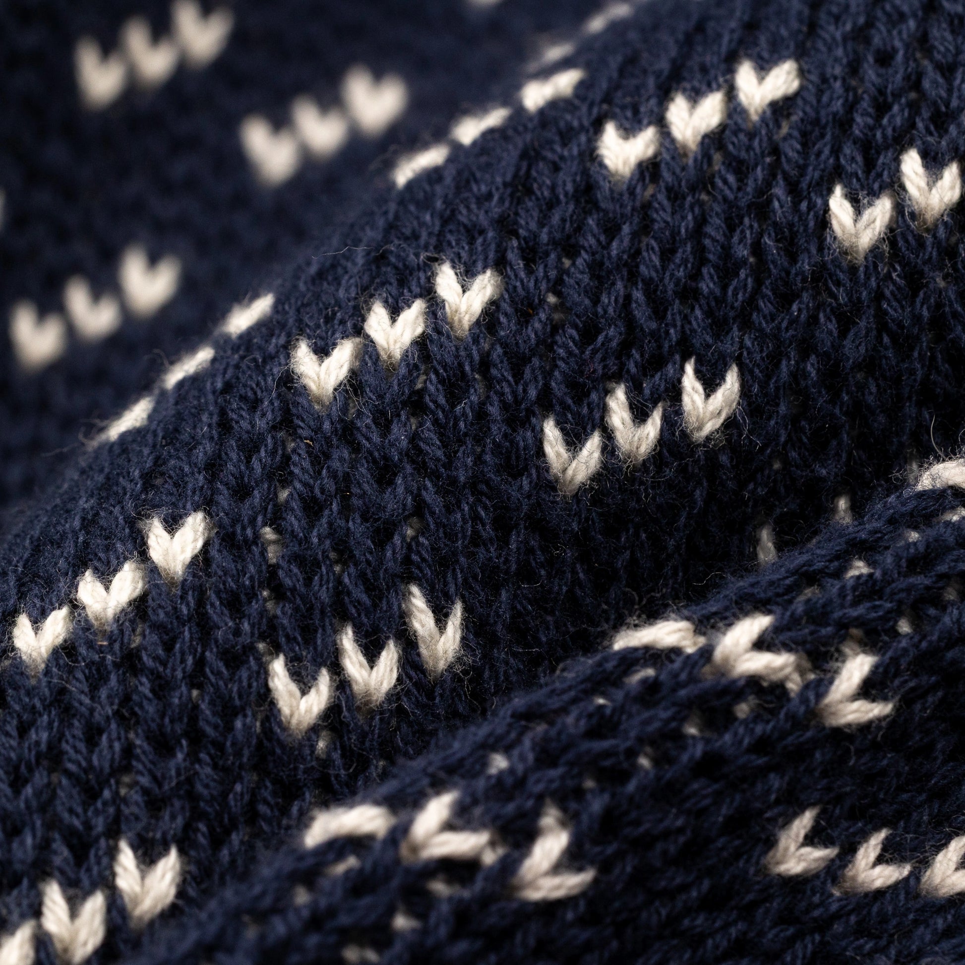 Extreme macro close-up of The 1926 Sweater fabric in navy and natural, showing the diagonal birdseye knit stitch detail with cream-colored V-shaped floats against a deep navy background.