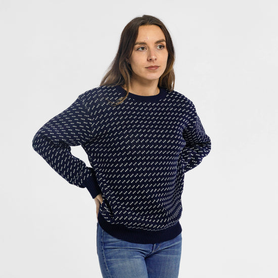 Woman wearing Bickford USA The 1926 Sweater in navy and natural, paired with light blue denim jeans, shown in a slightly turned pose with one hand on hip against a light gray background.