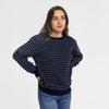 Woman wearing Bickford USA The 1926 Sweater in navy and natural, paired with light blue denim jeans, shown in a slightly turned pose with one hand on hip against a light gray background.