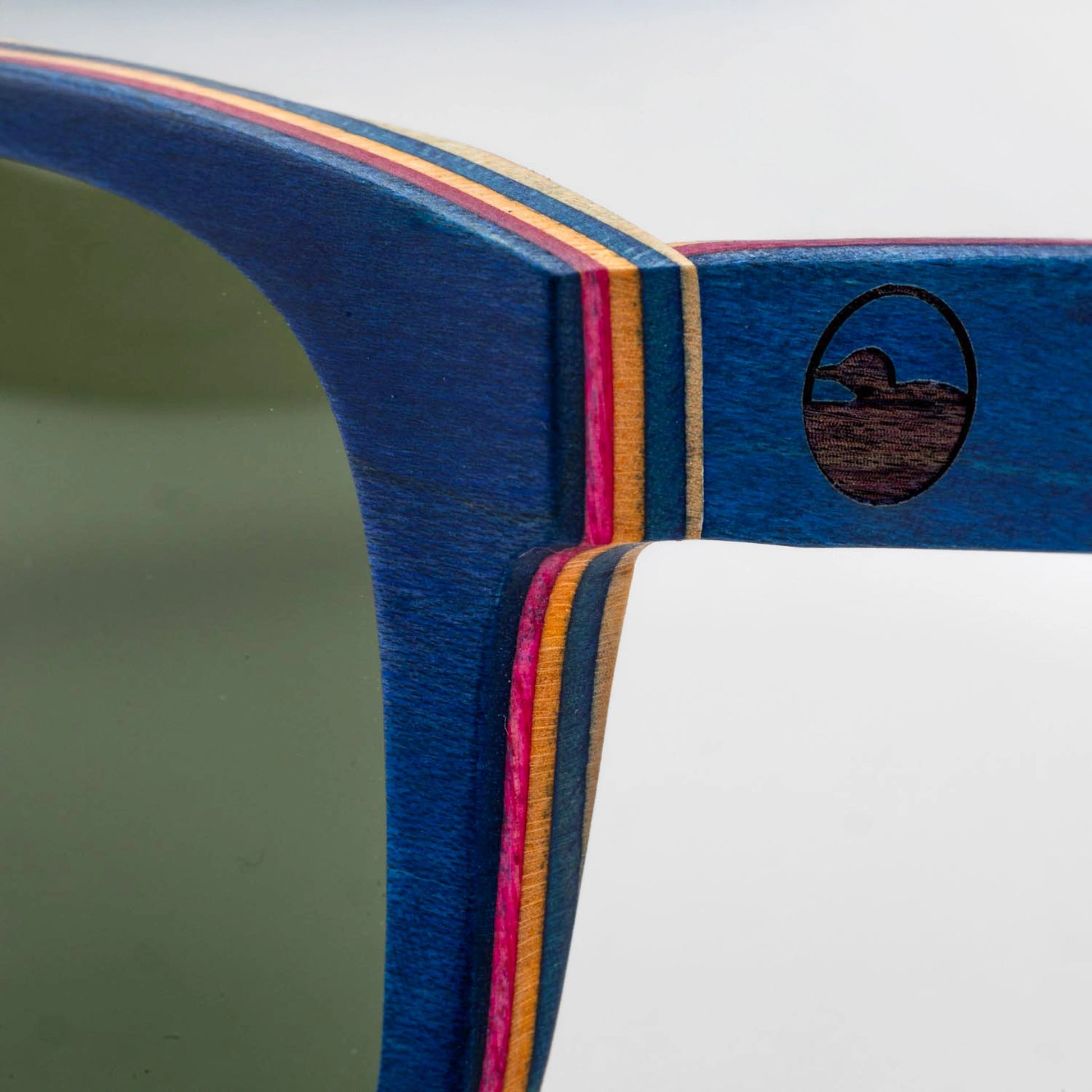 Close-up of the Bickford USA Timberline Full-Frame Sunglasses temple in deep blue, showing the layered skate-deck wood and engraved loon logo.