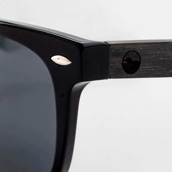 Close-up of the Bickford USA Timberline Full-Frame Sunglasses temple in midnight black, showing the wood temple inlay and engraved loon logo.