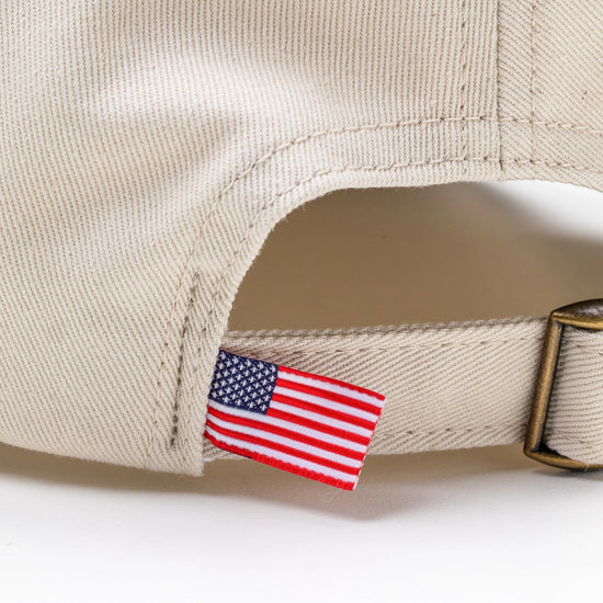 Close-up of American flag tag and antique brass buckle strap on Bickford Natural chino cap