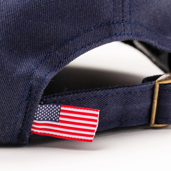 Close-up of American flag tag and antique brass buckle strap on Bickford Navy chino cap