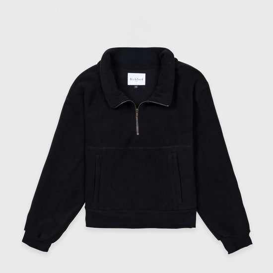 Bickford USA Women's Cropped Quarter-Zip fleece pullover in solid black, laid flat on a light gray background, showing the full front with a wide fold-over collar, brass quarter-zip closure, front kangaroo pocket, and ribbed hem and cuffs.