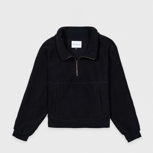Bickford USA Women's Cropped Quarter-Zip fleece pullover in solid black, laid flat on a light gray background, showing the full front with a wide fold-over collar, brass quarter-zip closure, front kangaroo pocket, and ribbed hem and cuffs.
