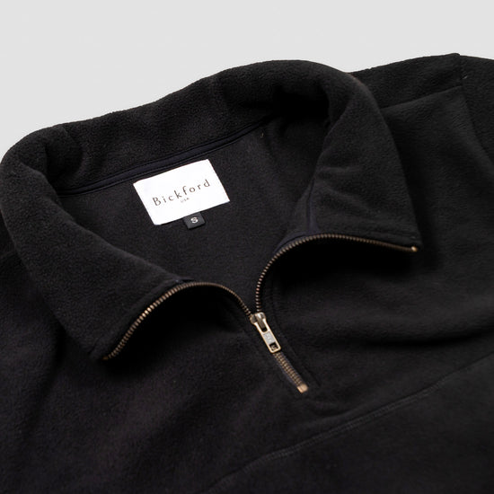 Close-up detail of the black Women's Cropped Quarter-Zip showing the open fold-over collar with the Bickford USA label and size tag visible inside, and the brass zipper pull partially unzipped.