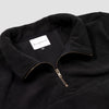 Close-up detail of the black Women's Cropped Quarter-Zip showing the open fold-over collar with the Bickford USA label and size tag visible inside, and the brass zipper pull partially unzipped.