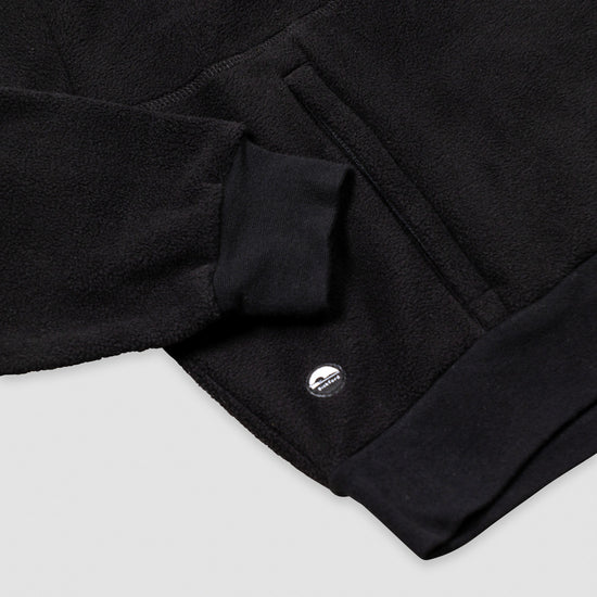 Close-up of the lower hem and kangaroo pocket area of the black Women's Cropped Quarter-Zip, showing the ribbed black hem band, the pocket opening with a knit tab detail, and the small circular Bickford logo patch.