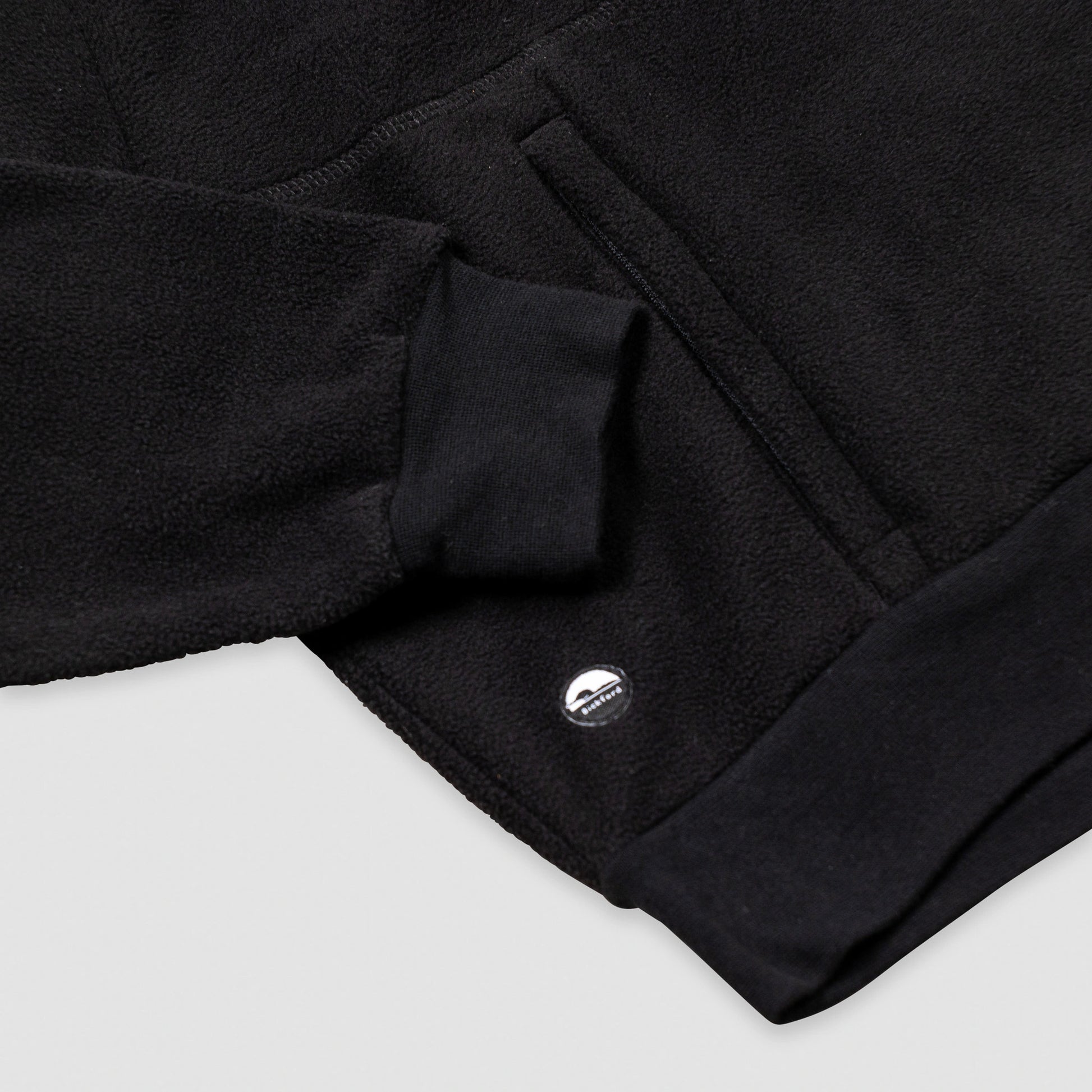 Close-up of the lower hem and kangaroo pocket area of the black Women's Cropped Quarter-Zip, showing the ribbed black hem band, the pocket opening with a knit tab detail, and the small circular Bickford logo patch.