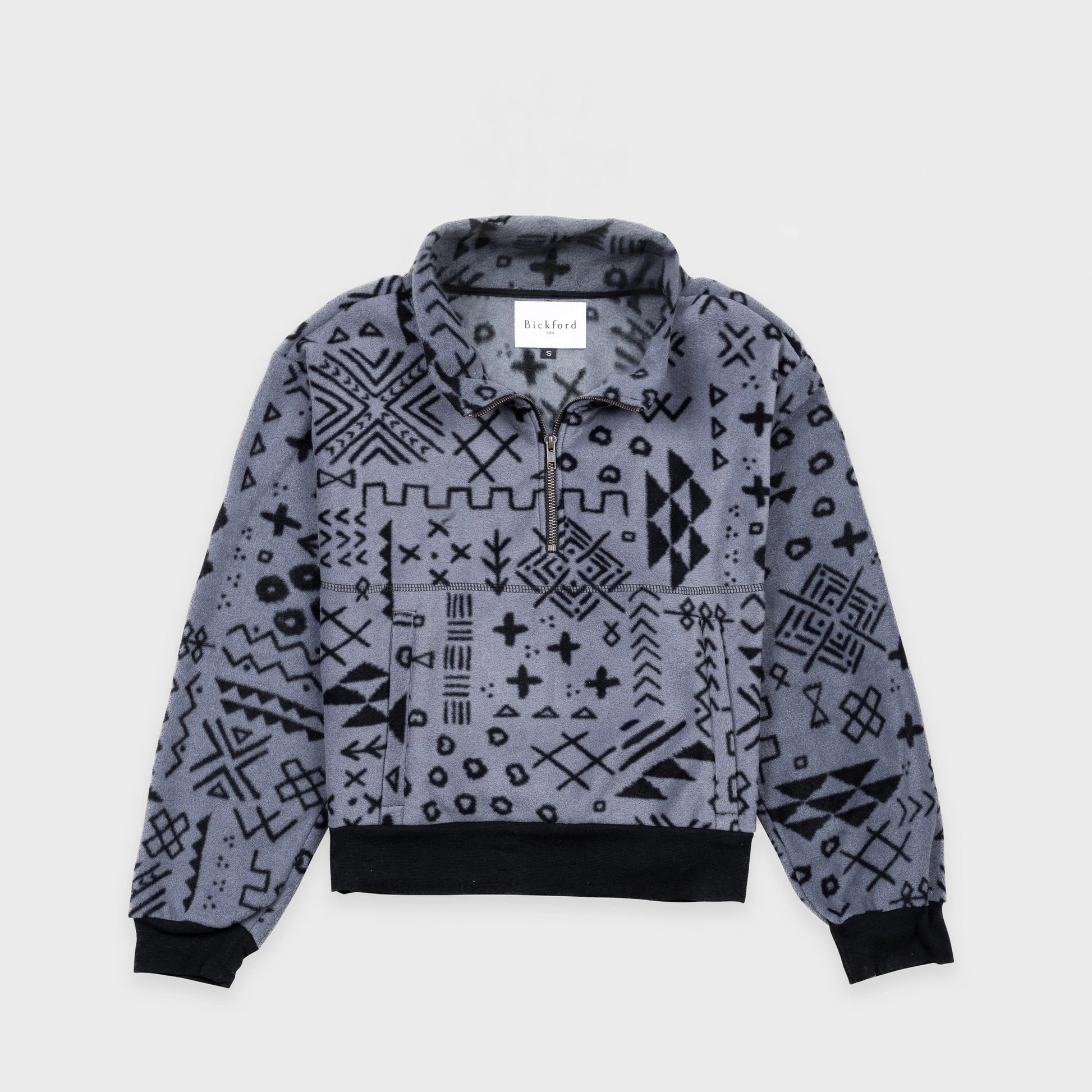 Bickford USA Women's Cropped Quarter-Zip fleece pullover in the Boulder colorway, laid flat on a light gray background, featuring an all-over black geometric tribal print on a grey background, with a wide fold-over collar, brass quarter-zip closure, front kangaroo pocket, and contrasting black ribbed hem and cuffs.