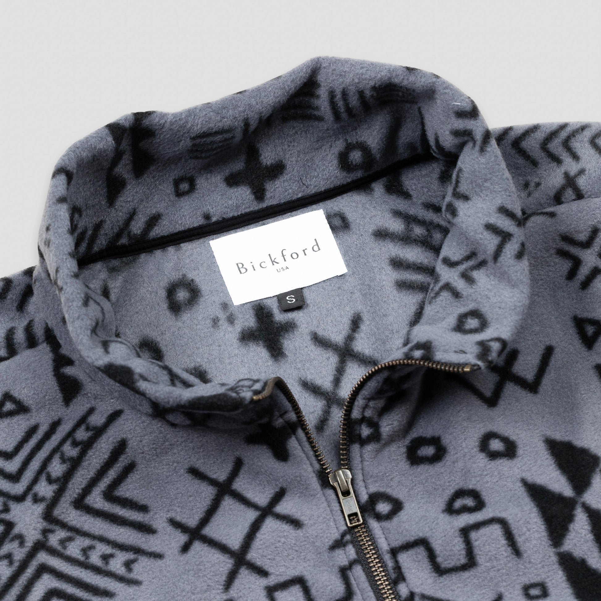 Close-up detail of the Boulder Women's Cropped Quarter-Zip showing the open fold-over collar with the Bickford USA label and size tag visible inside, and the brass zipper pull partially unzipped against the grey and black geometric tribal print.