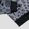 Close-up of the lower hem and kangaroo pocket area of the Boulder Women's Cropped Quarter-Zip, showing the contrasting black ribbed hem band, the pocket opening with a knit tab detail, and the small circular Bickford logo patch against the grey and black geometric print.