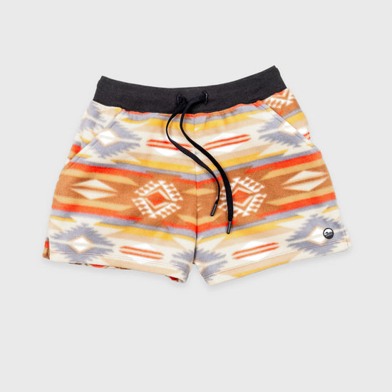 Bickford USA women's fleece shorts in the Heritage Trail colorway — a Southwestern-inspired pattern in warm tones of tan, rust, orange, gold, cream, and slate blue — flat lay front view, featuring a black ribbed elastic waistband, drawstring, and side hand pockets, against a light gray background.