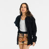 Woman wearing the Bickford USA Heritage Trail colorway women's fleece shorts paired with a white tank top and an open black Bickford button-down overshirt, smiling and facing forward, against a white background.