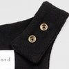 Close-up detail of the black Youth Overalls showing the adjustable shoulder strap with two brass snap closures and the Bickford USA label partially visible at the back of the neckline.