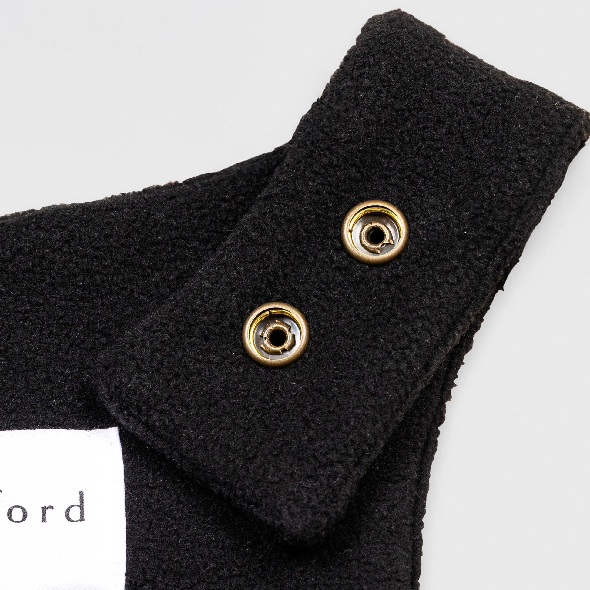 Close-up detail of the black Youth Overalls showing the adjustable shoulder strap with two brass snap closures and the Bickford USA label partially visible at the back of the neckline.