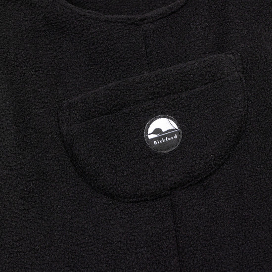 Close-up of the chest bib pocket on the black Youth Overalls showing the circular woven Bickford mountain logo patch centered on the pocket.